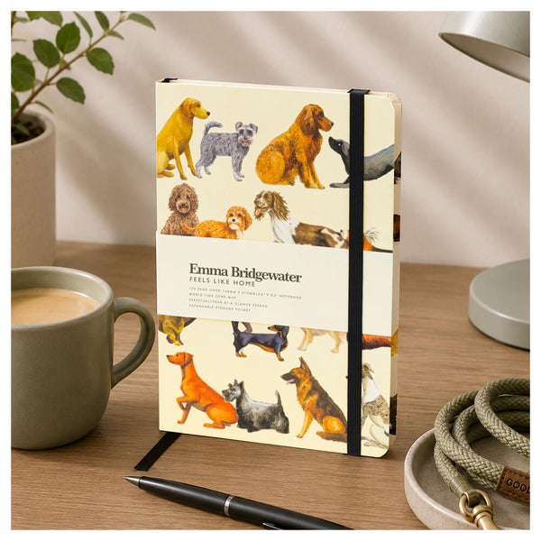 Notebook by Emma Bridgewater featuring dogs on the cover and an elastic strip.  Shown on a brown table and a drink in a grey cup.