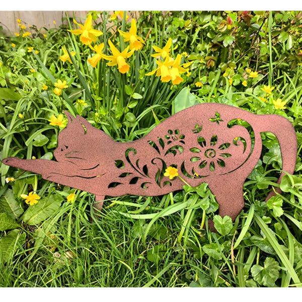 Rustic bronze metal cat garden decoration with grass and flowers.