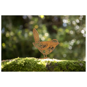 A metal fence decoration in the shape of a bird with cut-out floral details, placed on a mossy tree branch.