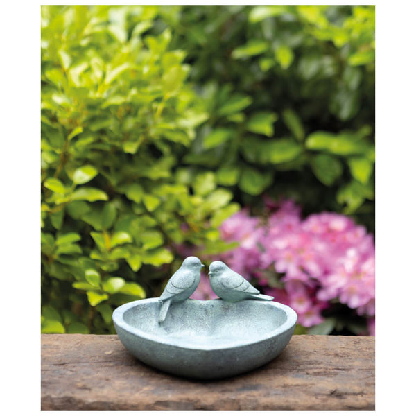 Decorative resin bowl with two birds on a wooden surface with greenery and flowers in the background