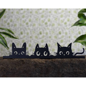 Three black cat cutouts on a wooden surface with a polka dot background