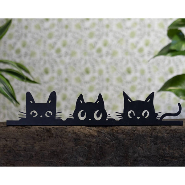 Three black cat cutouts on a wooden surface with a polka dot background