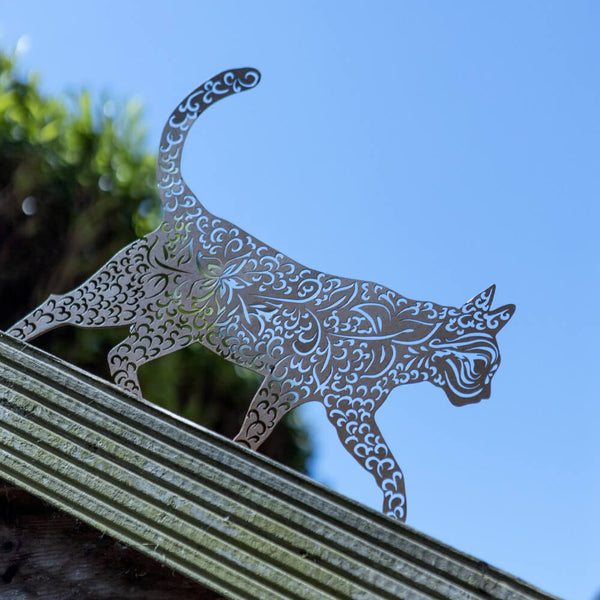 Decorative metal cat sculpture on a garden bench with a blue sky background