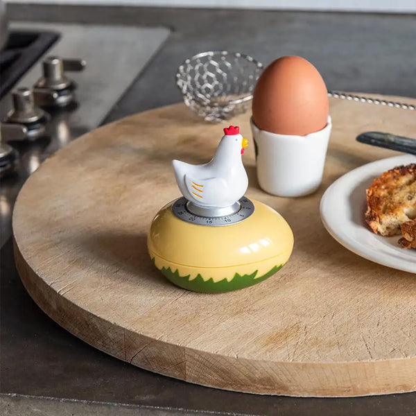 A chicken-shaped mechanical kitchen timer on a wooden surface, with a yellow and white body and a red comb.