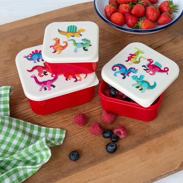Three red snack boxes with dinosaur designs on a wooden surface with berries.