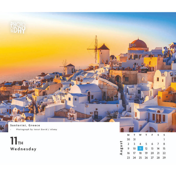 A wall calendar page showing a Santorini, Greece landscape photograph at sunset with white buildings, blue domes, and windmills. The left side includes the text 'Photo with the Day' and 'Santorini, Greece', with '11th Wednesday' in large type.