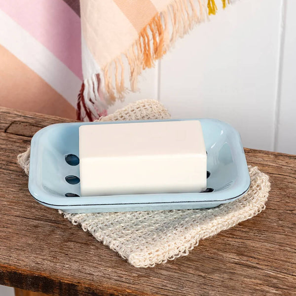 Bar of soap in a blue soap dish on a wooden surface with a plaid blanket in the background