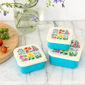 Three rectangular snack boxes with a wild flowers print on the lids, displayed on a marble surface.