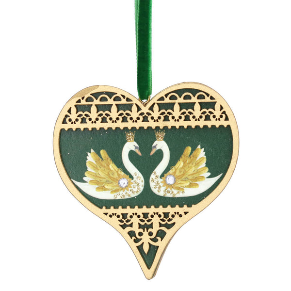 A heart-shaped wooden Christmas ornament featuring two swans facing each other on a dark green background, with a gold-colored laser-cut lace border and a green hanging ribbon.
