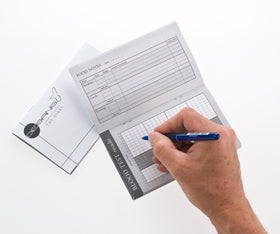 A person's hand writing in a blood test diary with a pen, showing the diary's two-page layout designed for logging health information.