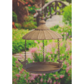 A hanging metal bird feeder with a decorative parasol top and two birds perched on the sides, set against a blurred garden background.